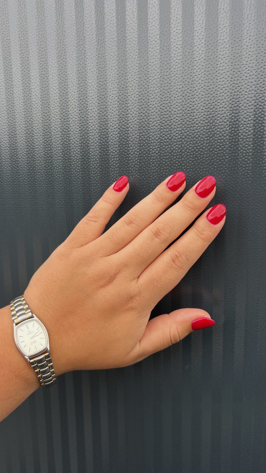 Glanzende rode nagels, hand met zilveren horloge